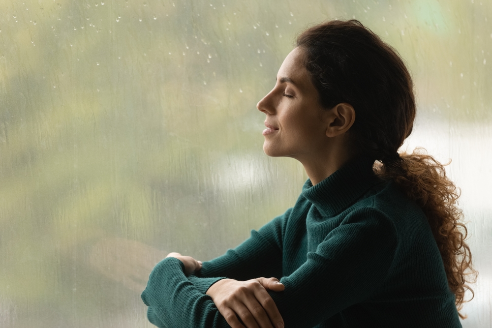 woman closing her eyes by rainy window